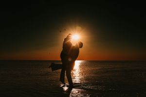 Silhouette of a couple embracing on a beach at sunset with sun flare.