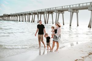 Family walking along a beach with a wooden pier stretching into the distance.