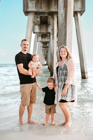 Family enjoying time together in the shallow waters beneath a large concrete pier structure.