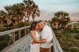 A couple embraces on a beachside walkway during golden hour with tropical palm trees in the background.
