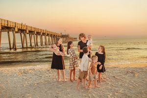 Group enjoying sunset at beach pier with golden light reflecting on ocean waves.