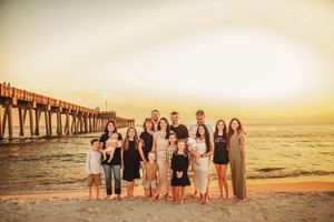 Group photo of people standing on beach with wooden pier in background at sunset.