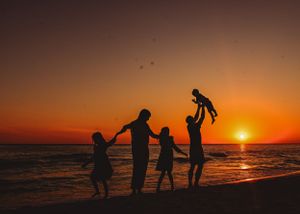 Silhouette of family playing on beach at sunset with dramatic orange sky.
