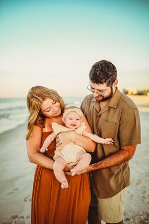 Family enjoying sunset moment together on sandy beach with teal and orange tones.