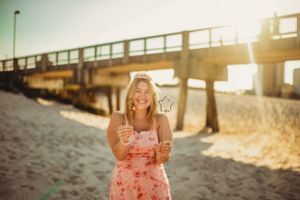 A beach pier stretches into the ocean at golden hour with sunlight streaming through.