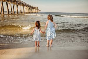 Children playing and splashing in ocean waves near a wooden pier at sunset.