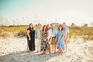 Family group wearing coordinated pastel outfits standing on sand dunes at the beach.