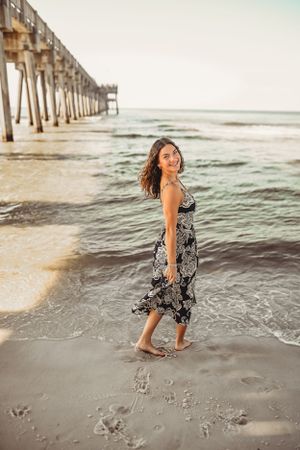 Person splashing and playing in ocean waves near a wooden pier at sunset.