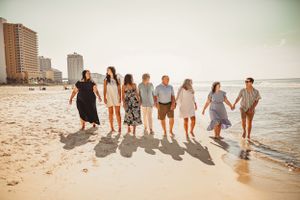 Group walking along shoreline at sunset casting long shadows on sandy beach.