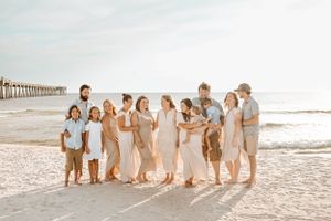 Large group in coordinated outfits poses together on sunny beach near pier.