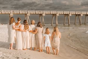Group standing together facing ocean at beach with pier in background.