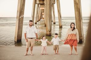 Family portrait under a beach pier with ocean waves in the background.