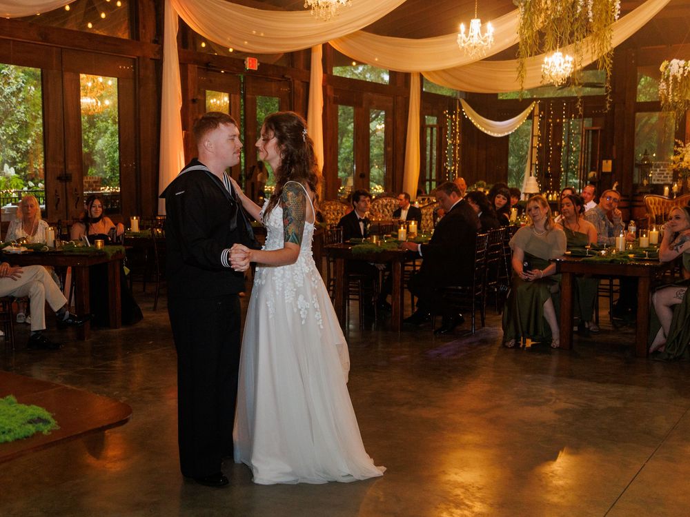 Bride and groom share first dance at elegant indoor wedding reception with guests seated at candlelit tables.