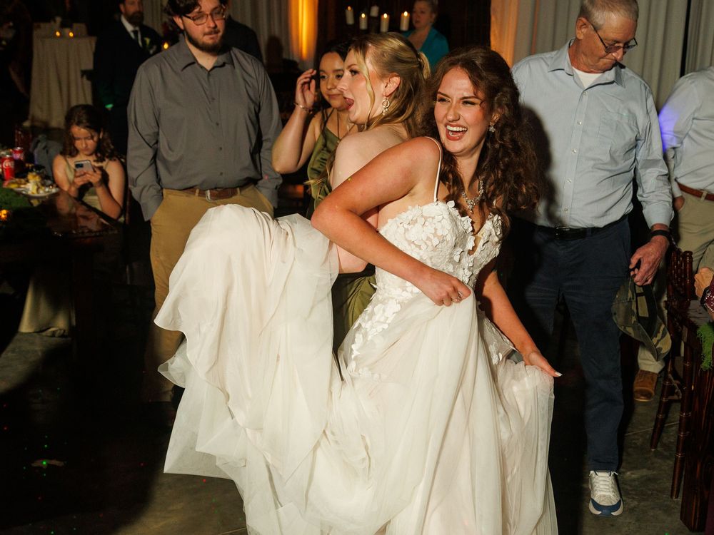 Two brides in white gowns dancing joyfully together at a wedding reception celebration.