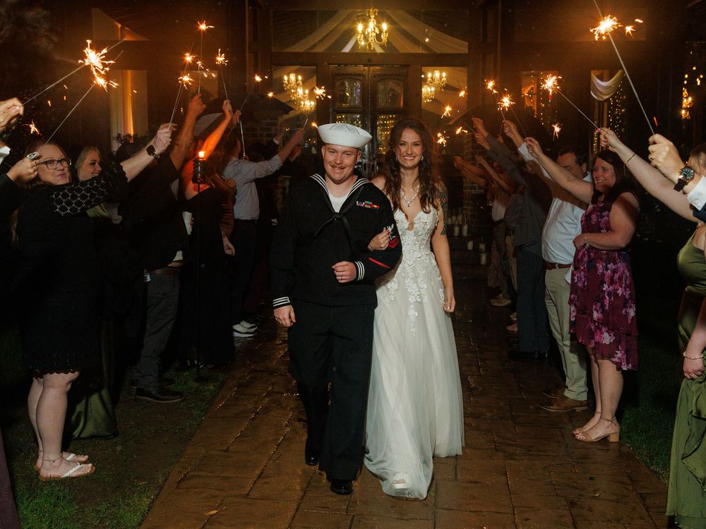 Navy groom and bride walk through sparkler exit at night wedding ceremony with guests lining path.