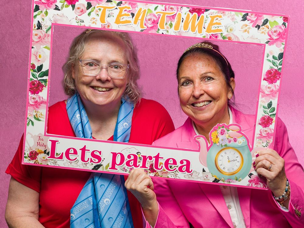 Two women smiling behind a floral Tea Time photo booth frame at a party celebration event.