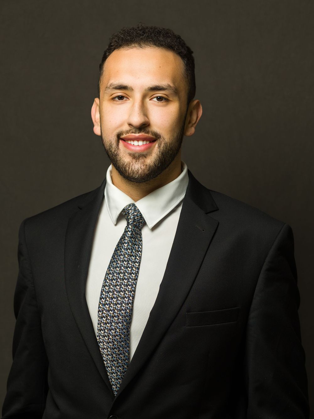 Professional studio portraits showing a person in a black suit and patterned tie against a dark background.