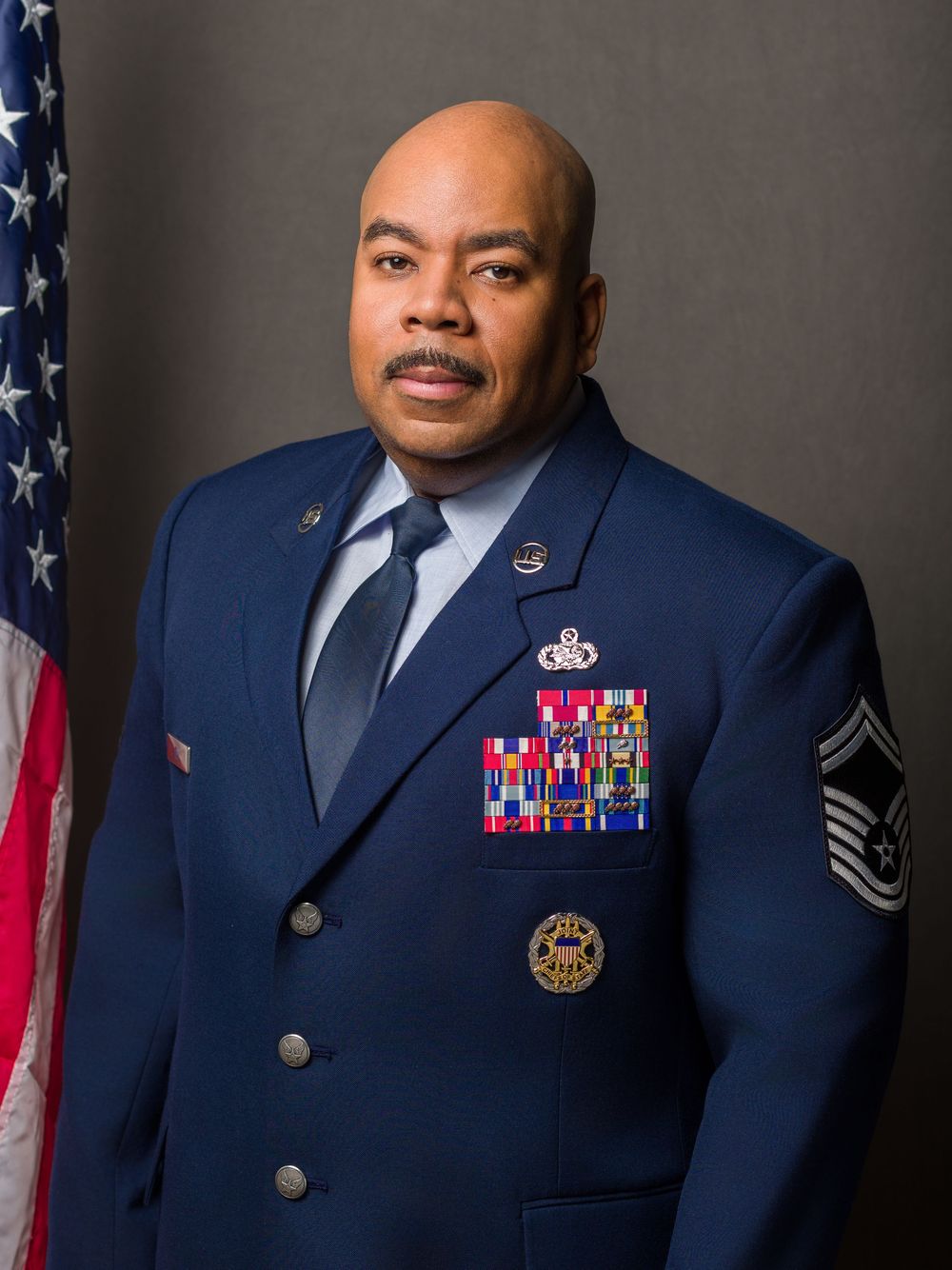U.S. Air Force service member in dress uniform poses for official military portrait with American flag background.