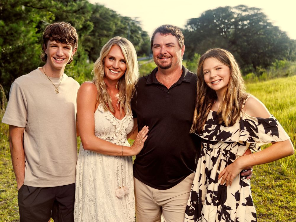 Family of four smiling outdoors in a lush green field during golden hour.
