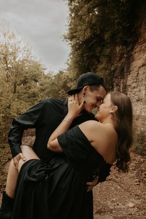 Romantic couple in black attire sharing intimate moment against rocky cliff.