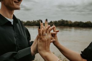 Close-up of hands showing engagement ring against water background.
