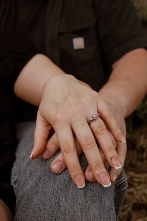Close-up of hands resting on denim with an engagement ring prominently displayed.