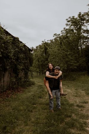 A couple playfully interacts in a scenic outdoor setting with trees in the background.