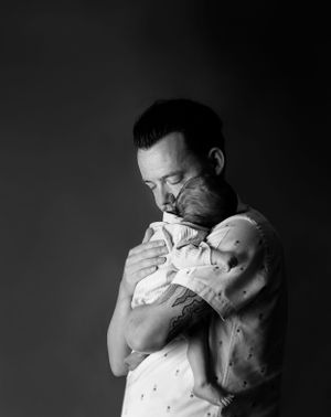 Dad cuddling newborn son in his arms, dad has tattoos on his arm