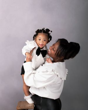 A heartwarming portrait of mom and baby wearing matching white outfits against a gray background.