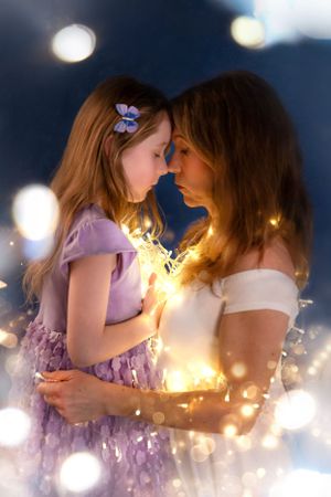 Dreamy mother and daughter portrait with bokeh lights and purple dress against dark blue background.