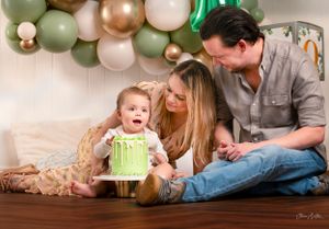 baby boy having his birthday cake with Mum and Dad sat with him during a cake smash