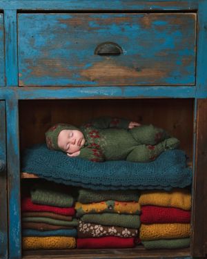 A vintage blue drawer with distressed paint contains folded colourful knit blankets and a cozy sleeping space for a baby.