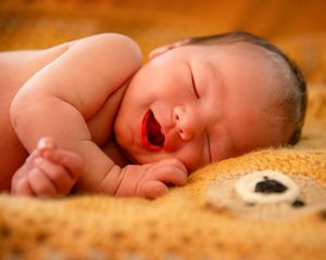 Peaceful newborn baby sleeping on textured gold blanket in warm light.
