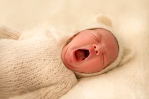 Sleeping newborn in soft white knit wrap captured in warm tones.