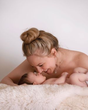 Parent shares a tender moment with newborn baby while laying on soft white fur blanket.