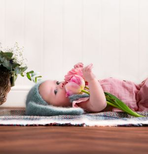 baby girl laying on a picnic blanket, smelling a flower, wearing baby blue bunny ears, baby props