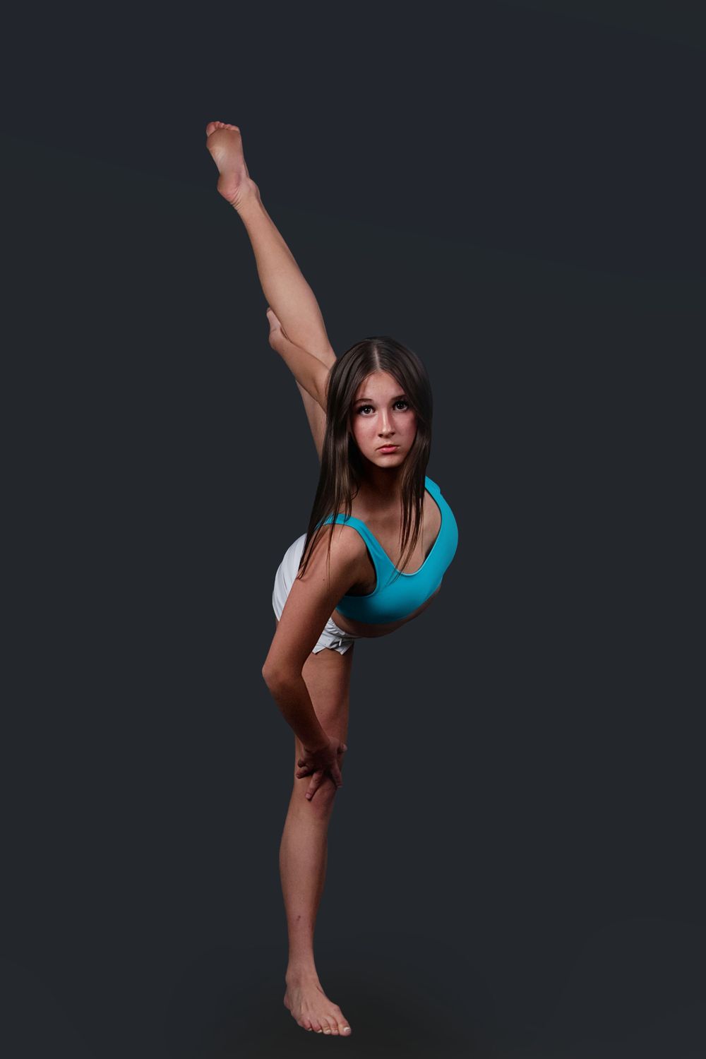 Young gymnast in blue leotard performing a standing split pose against a dark background.