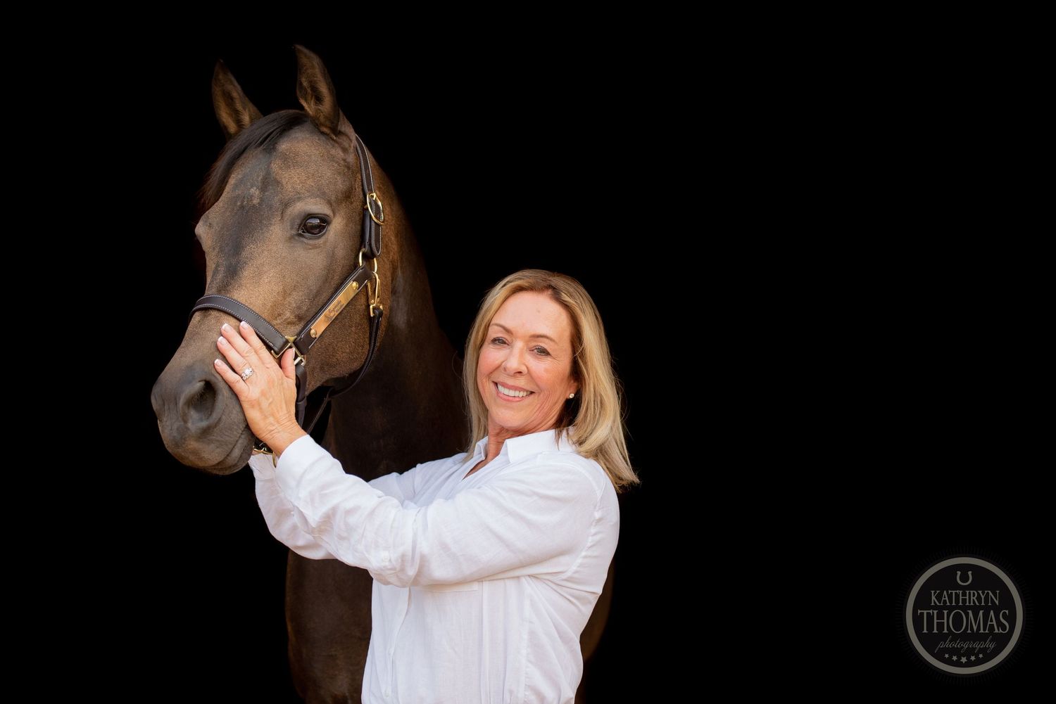 A dark horse and rider pose together against a dramatic black background.