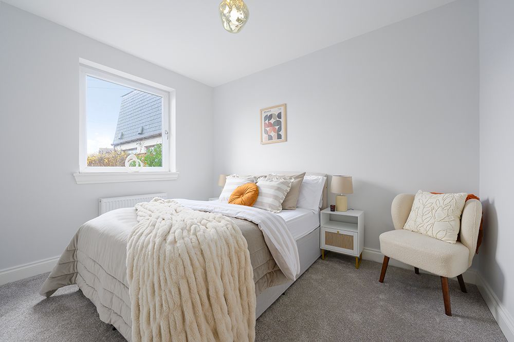 Modern white bedroom with minimal decor features plush bedding, hardwood floors, and natural light from a window.