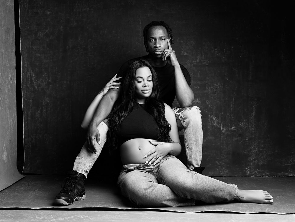 A black and white artistic portrait of a couple posing intimately against a dark backdrop.