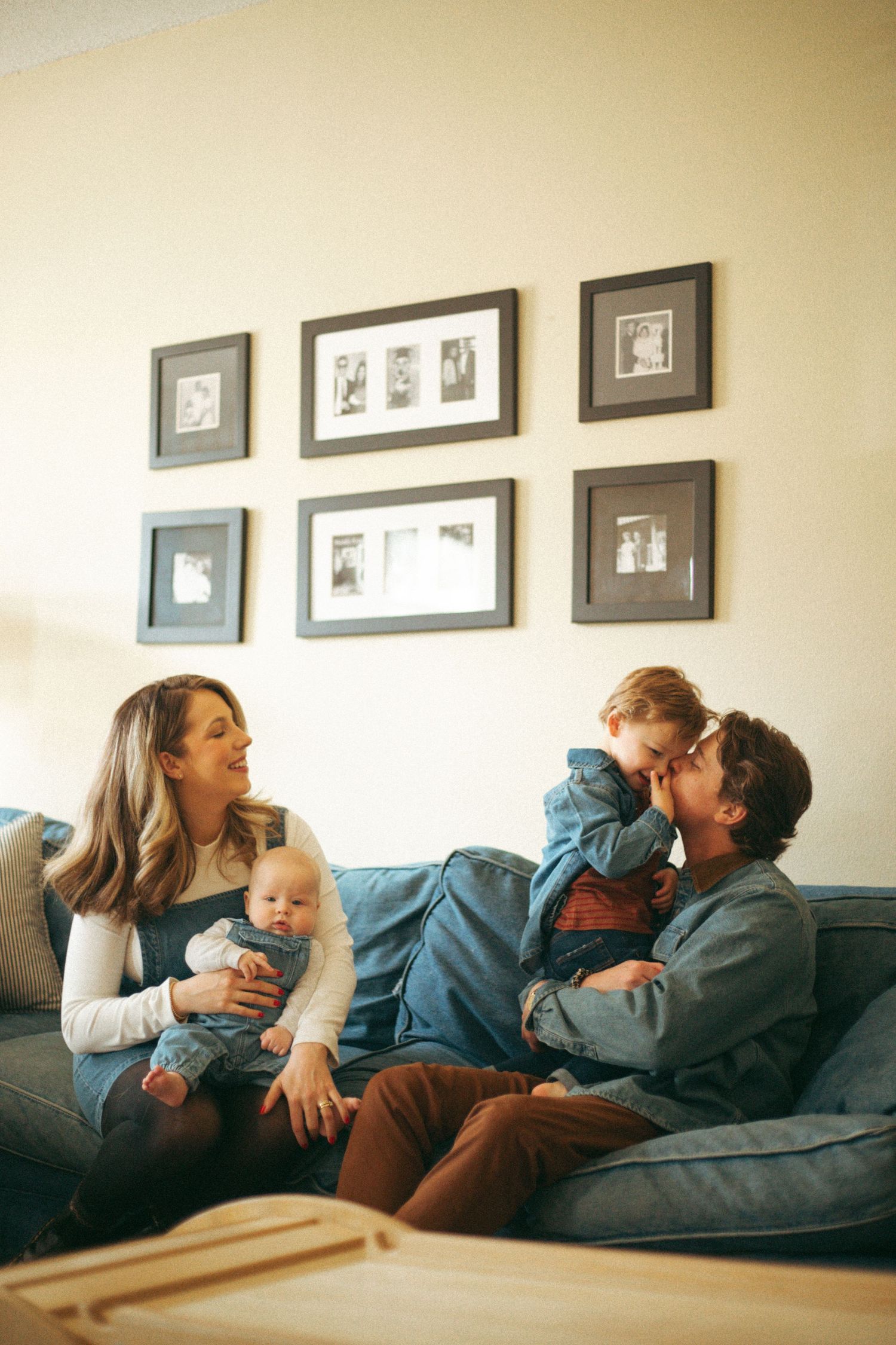 Candid family moment on grey couch with framed photos displayed on wall.