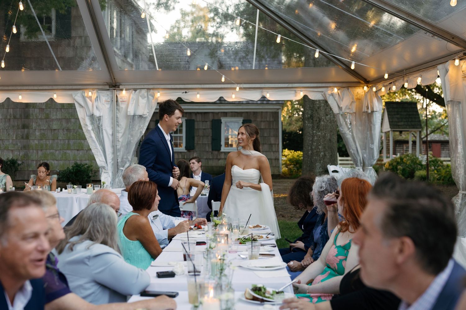 Wedding reception under a tent with string lights and elegant table settings.