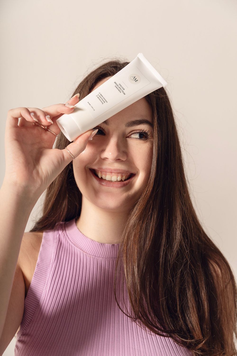 Person in pink sweater playfully poses with white skincare product tube across their face in series of photos.