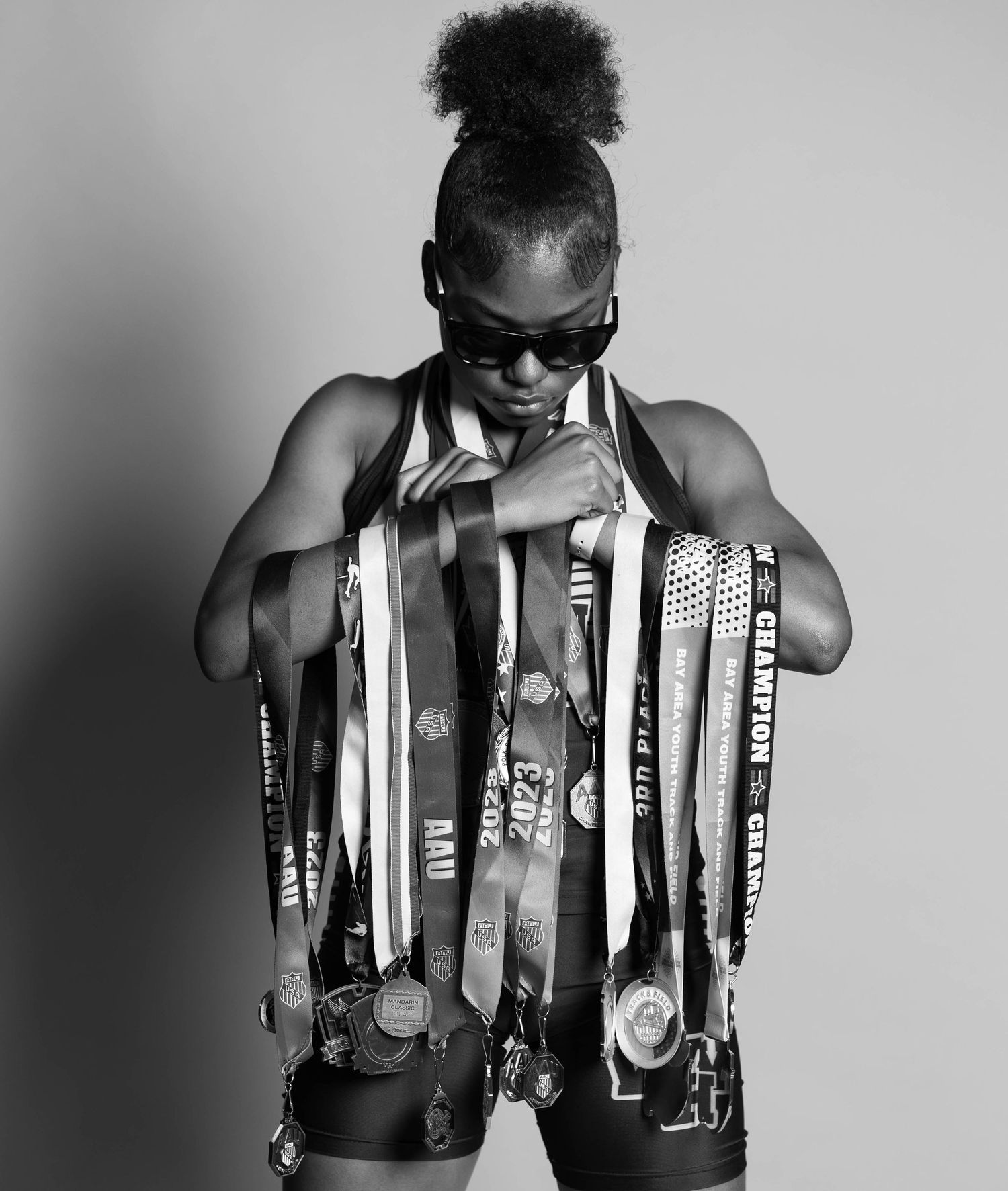 Black and white photo of an athlete wearing sunglasses displaying numerous championship medals and ribbons.