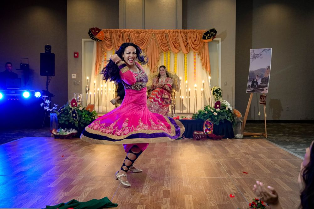 Festive wedding reception crowd dancing in colorful traditional attire under ballroom lighting.