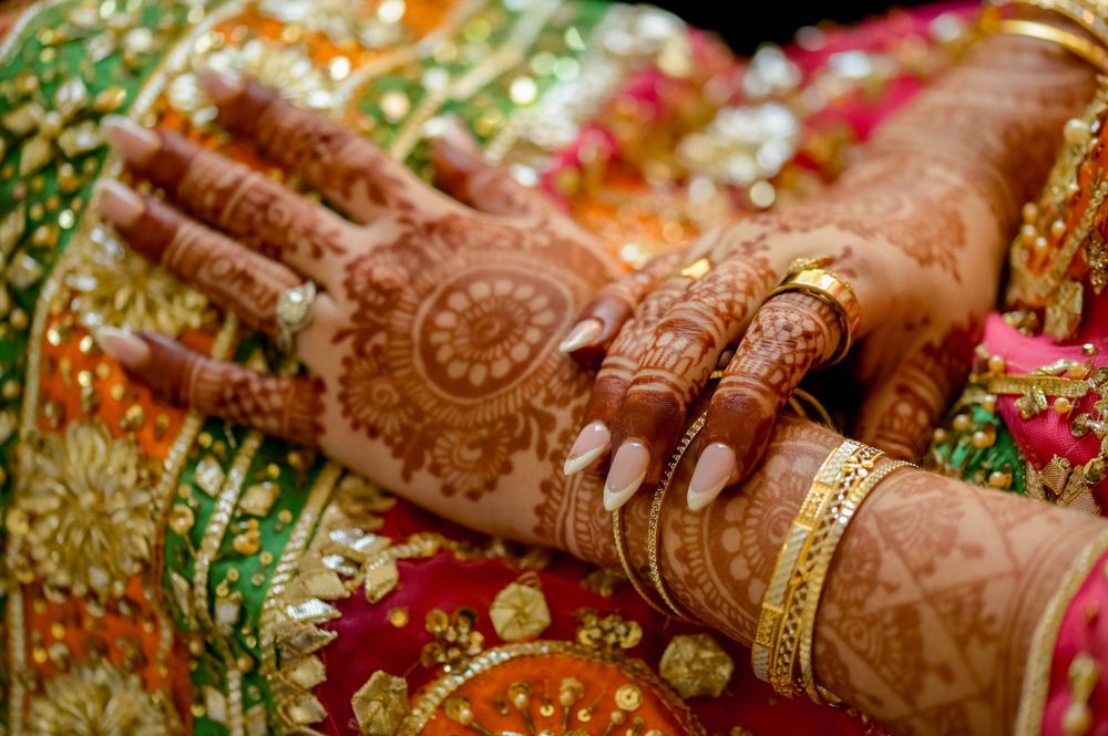 Detailed shot of mehndi adorned hands with gold bangles against colorful traditional fabric.