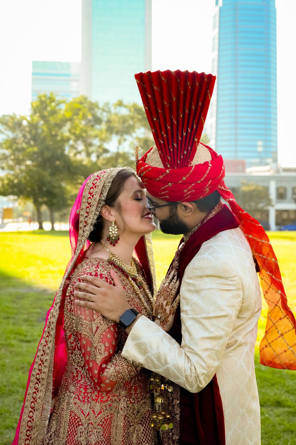 Couple in ornate South Asian wedding attire sharing tender moment on city sidewalk.
