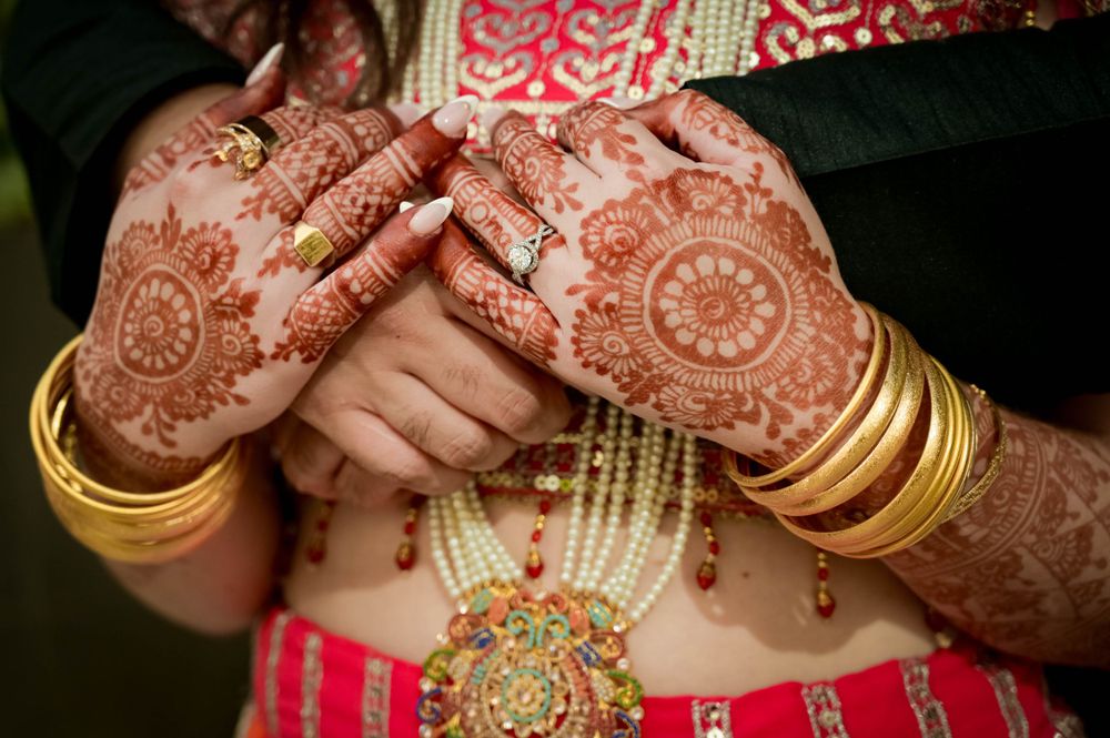 Close-up of henna decorated hands with gold bangles and traditional Indian jewelry.