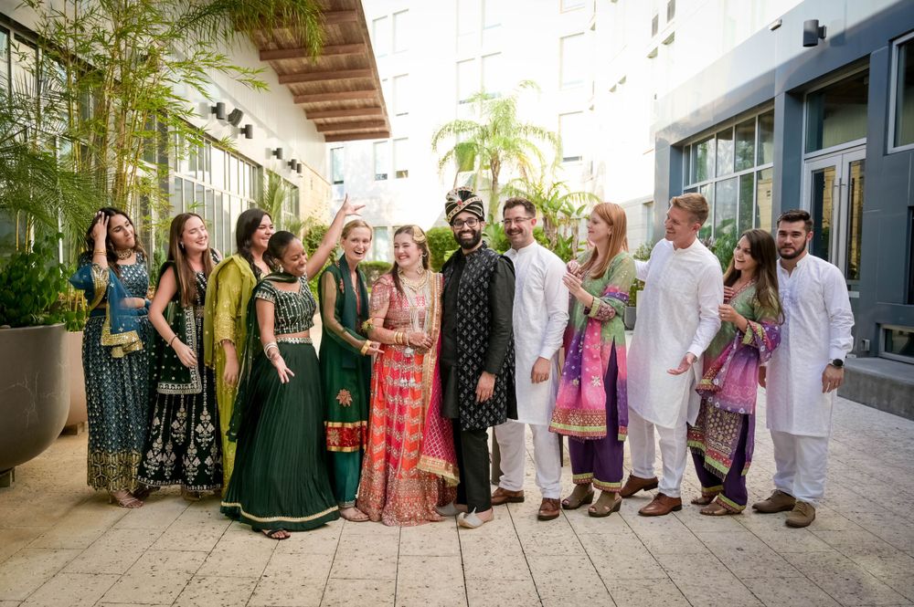 Group photo of wedding party in colorful Indian traditional attire standing in front of palm trees.