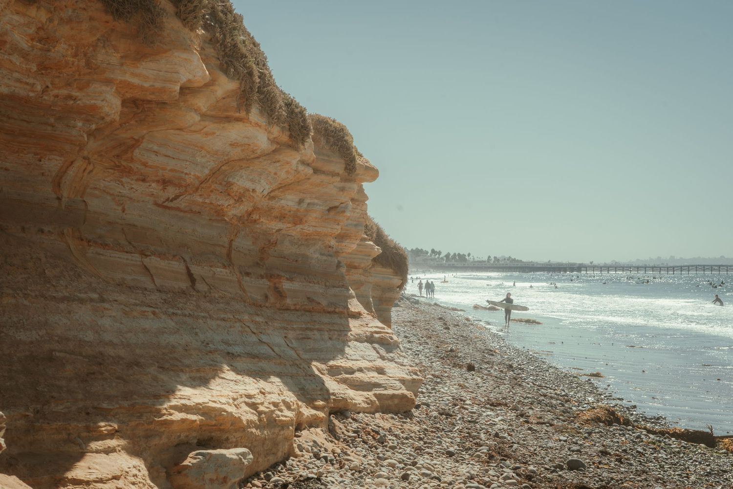 Cliffs and shoreline at tourmaline in San Diego. people walking on the beach and getting ready to paddle out to surf